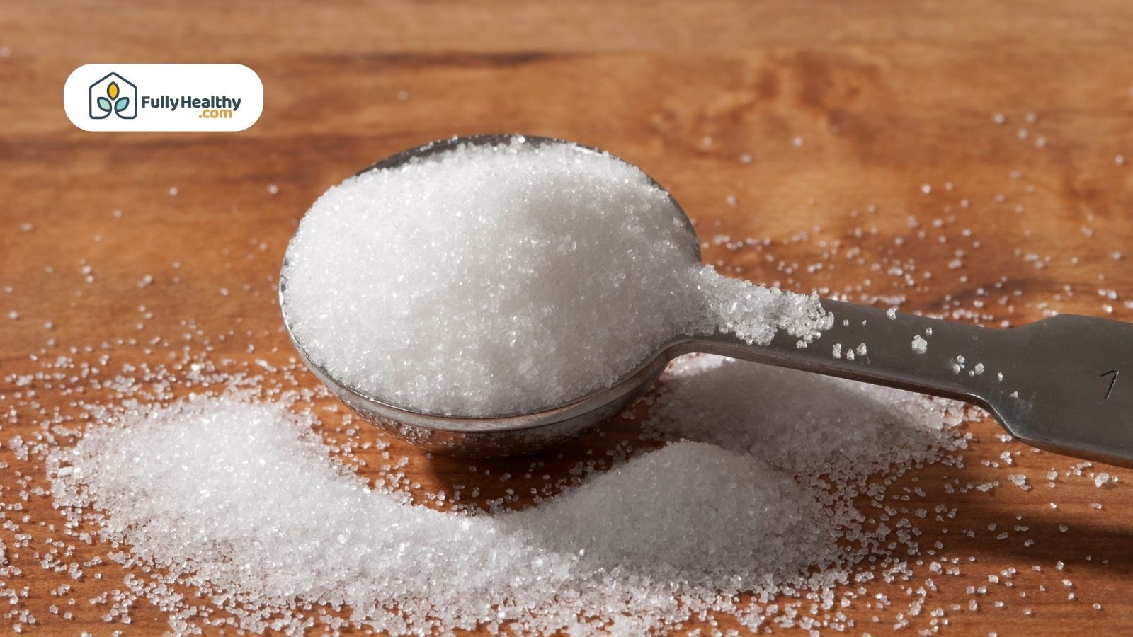 Granulated sugar in a metal teaspoon spilling on wooden table