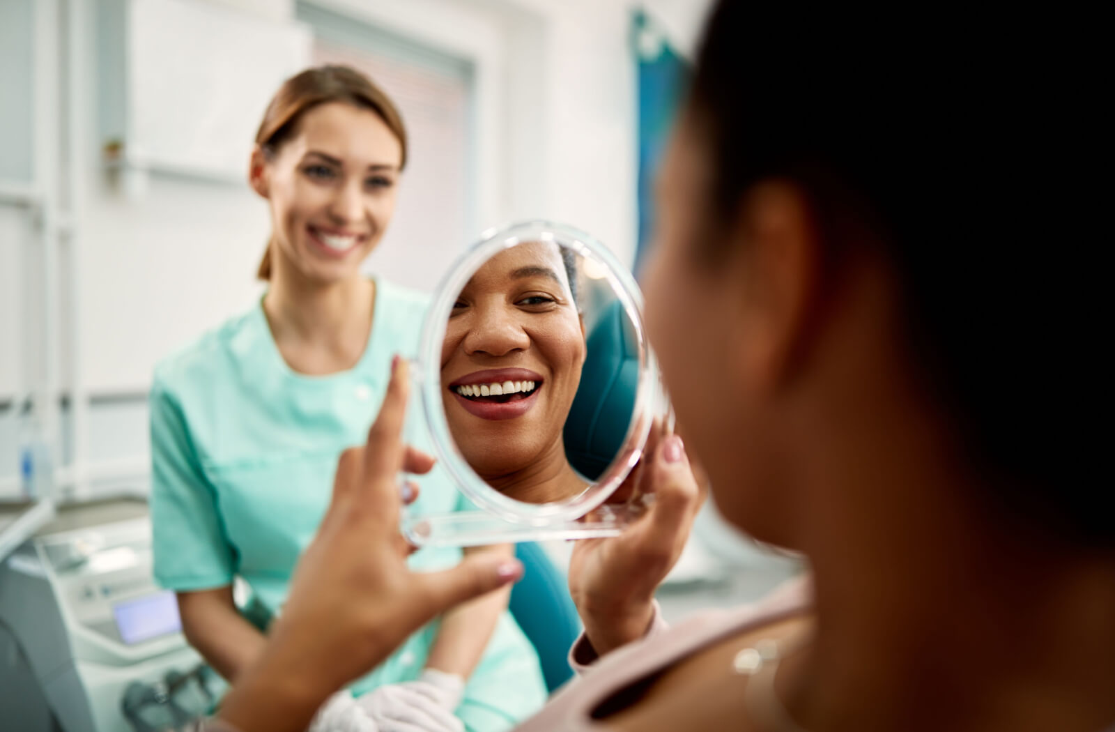 A patient happily examining the results of their dental implant procedure while a dentist smiles in the background.
