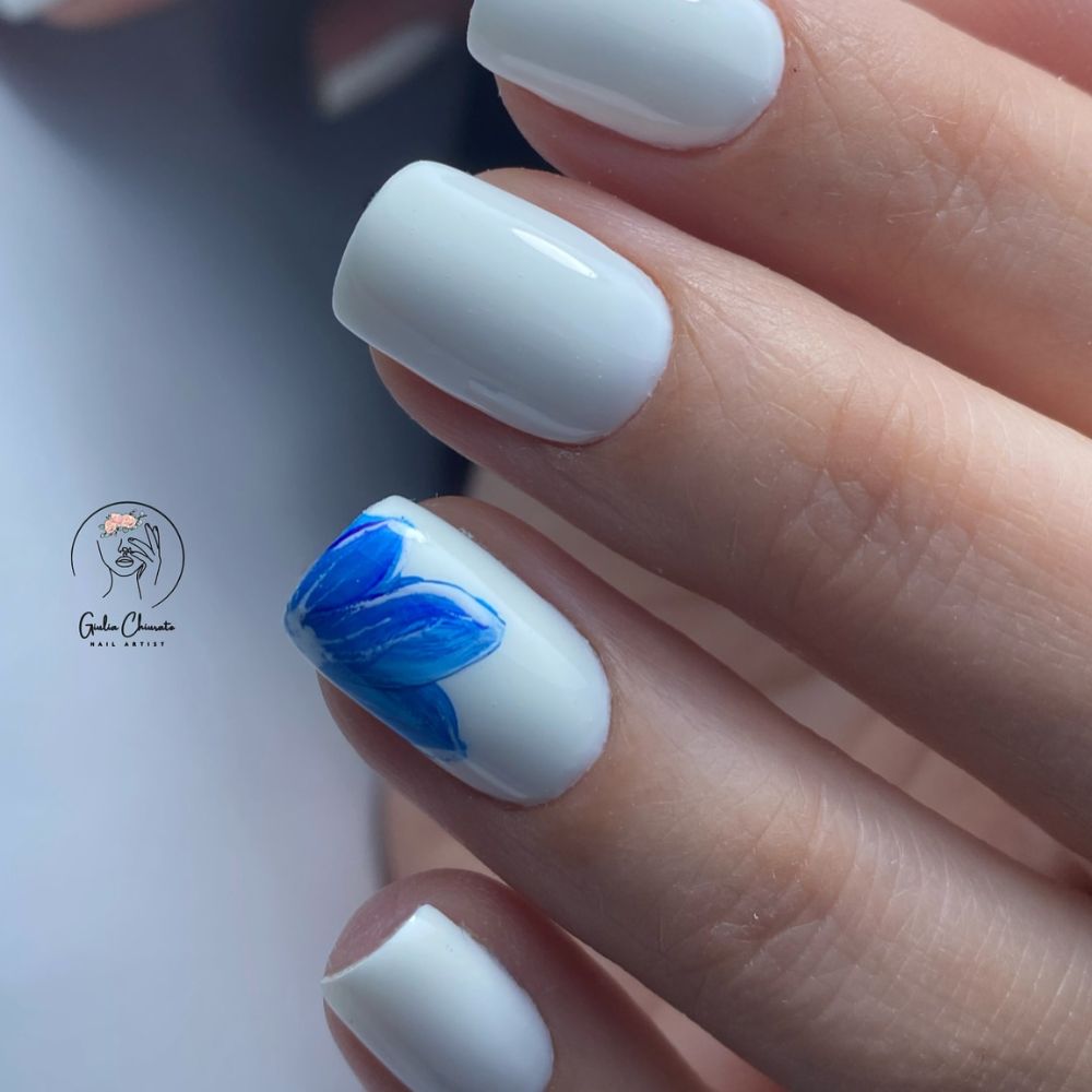 Close up of flowered short nail design with White nails with blue flower