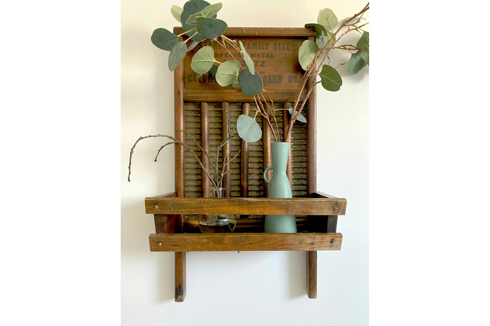 DIY reed diffuser sticks on a brown wooden wall mounted rack with green plant.