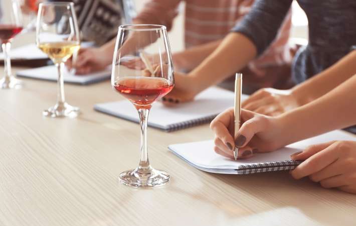 People writing in notebooks while trying out a rose and a white wine