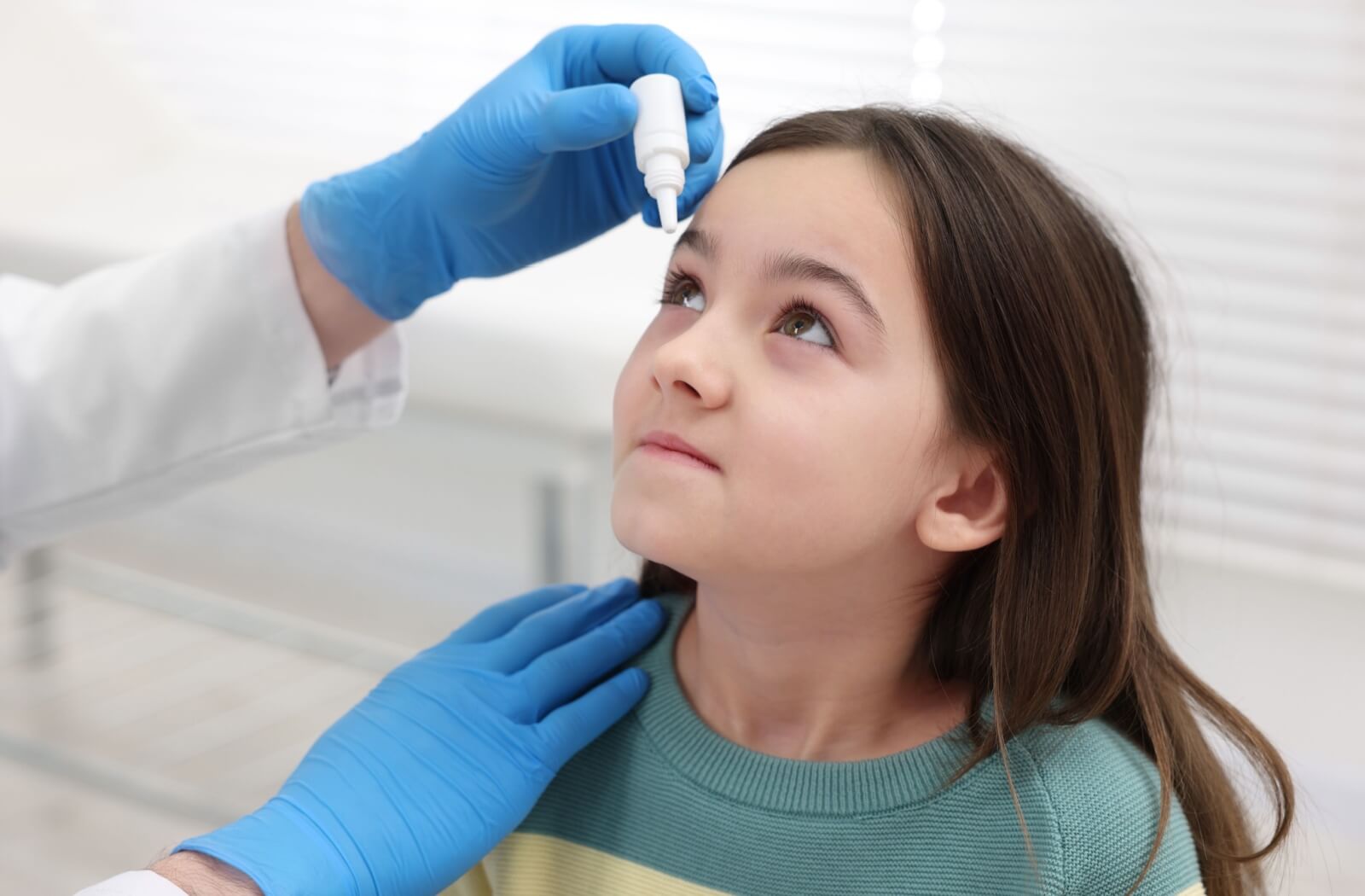 An eye doctor puts medicated eye drops into a child's eye.