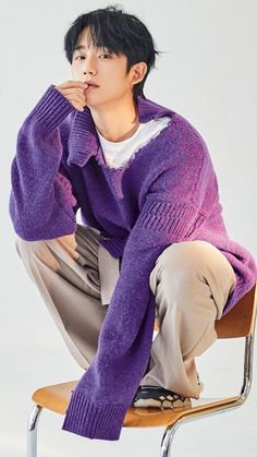 This contain Jung Hae In  sitting on top of a chair wearing a purple sweater and khaki pants