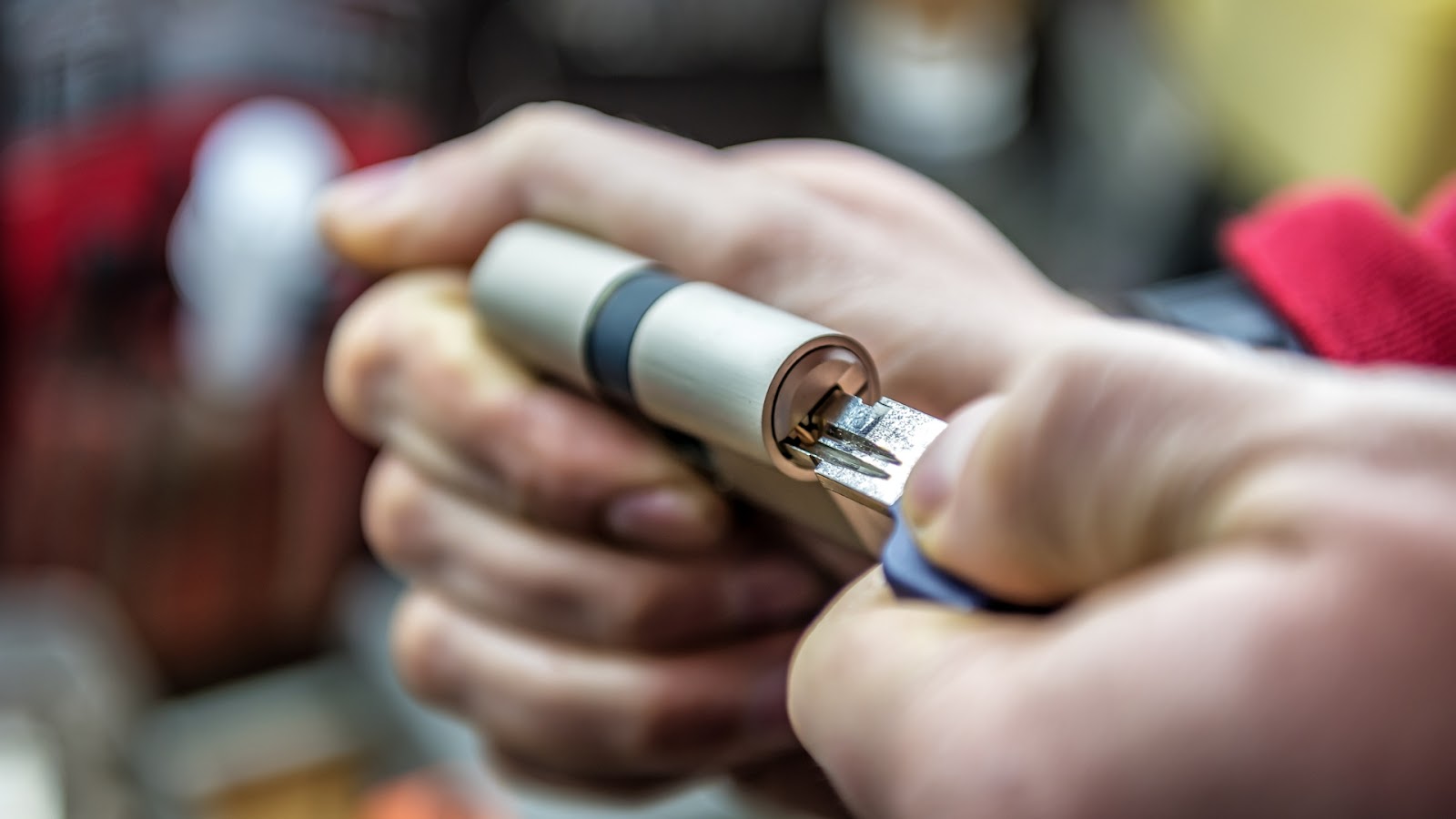 A hand holds a metal lock cylinder with a key inserted, showing the process of lock rekeying.