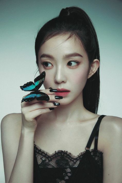 This contain Irene with black and blue nail polish holding a butterfly in her hand while looking at the camera