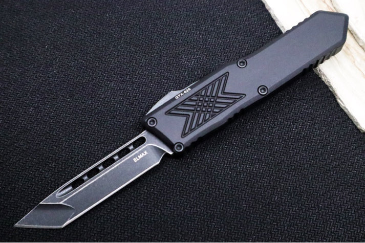 An image featuring the Guardian Tactical GTX-025 OTF in dark stonewash finish. The knife lays flat on a solid black and wood backdrop.