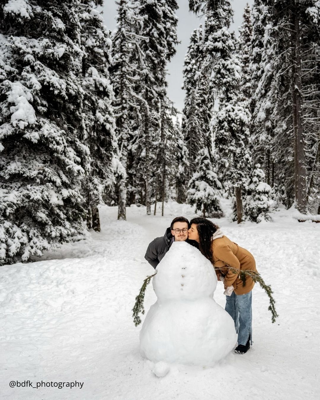 winter engagement photos girl is kissing boy near snowman