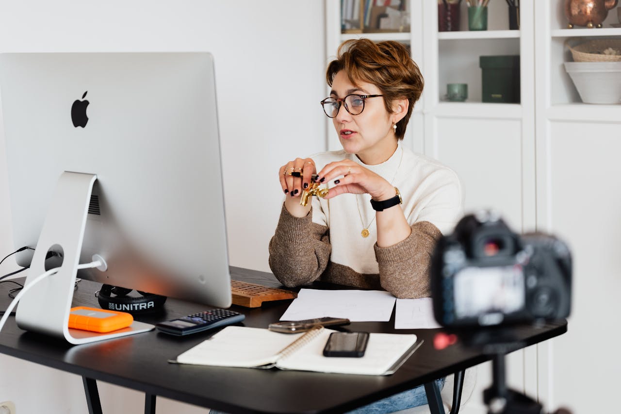 A professional woman actively participating in a video recording session showing how to create online courses at her desk equipped with a computer and office supplies in a modern workspace.