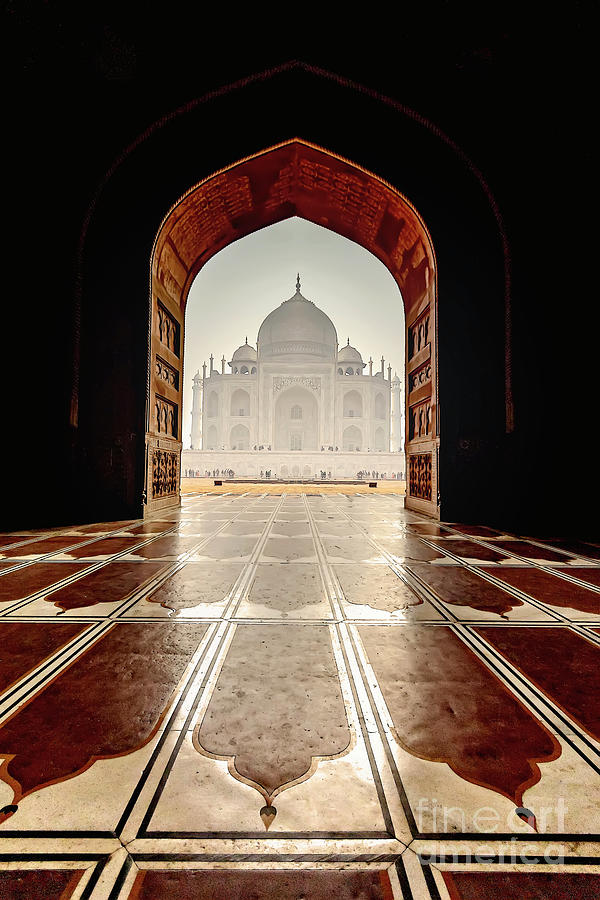 Through the intricately designed archway, the architectural masterpiece of the Taj Mahal in Agra emerges, with sunlight shimmering on the geometric patterned floor.