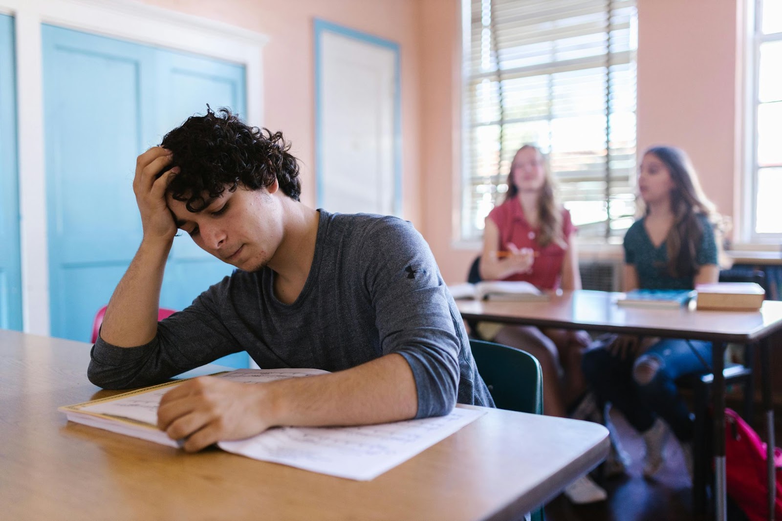 A student reading a book with two others talking behind him in a class