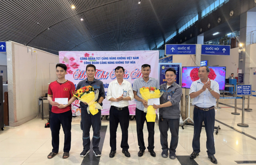 A group of men standing in a room with flowers and a bannerDescription automatically generated