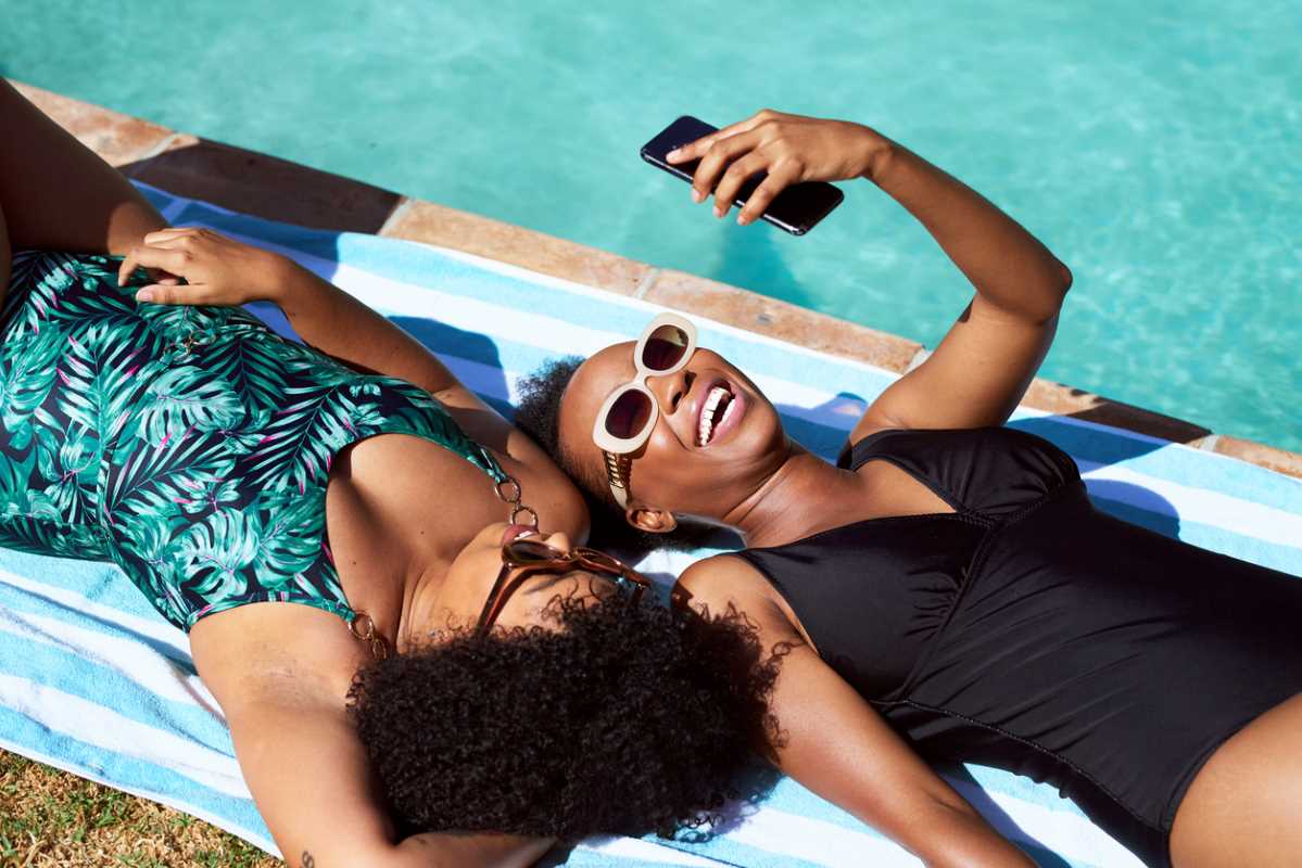 Two women lying beside a clean and crisp pool on a sunny day.