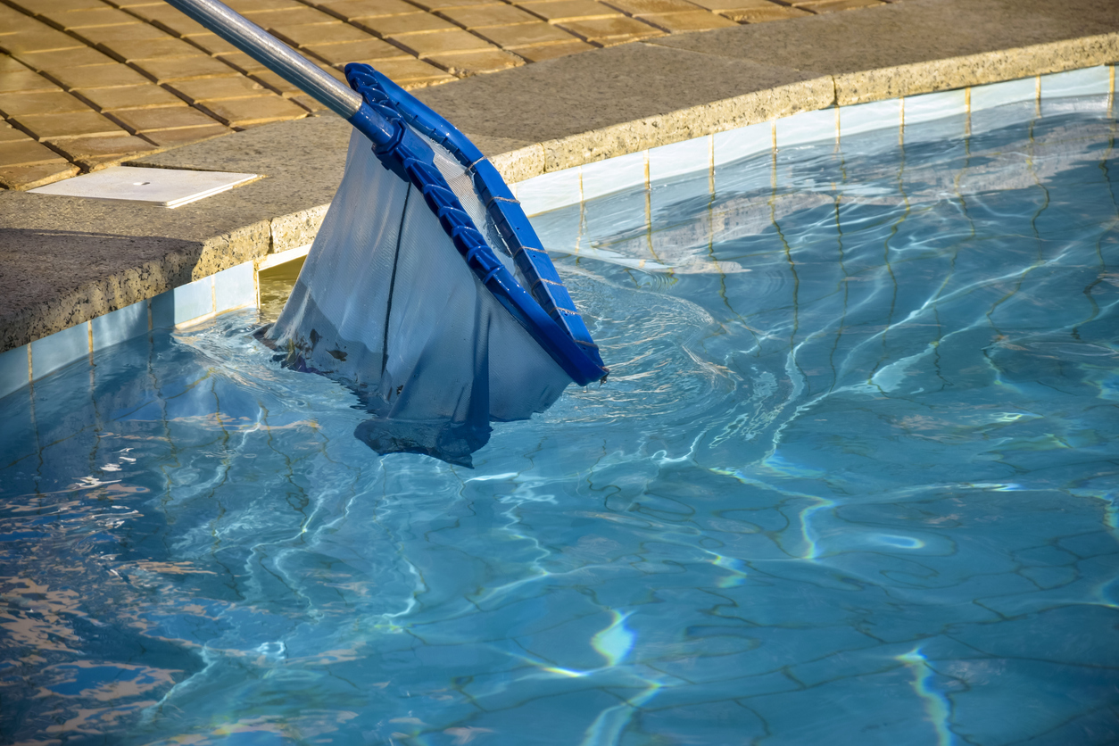 A person removes debris from pool water using a net.