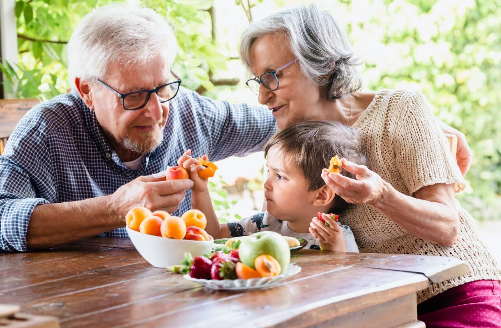 A senior couple enjoys a healthy snack of fresh fruit with their grandchild.