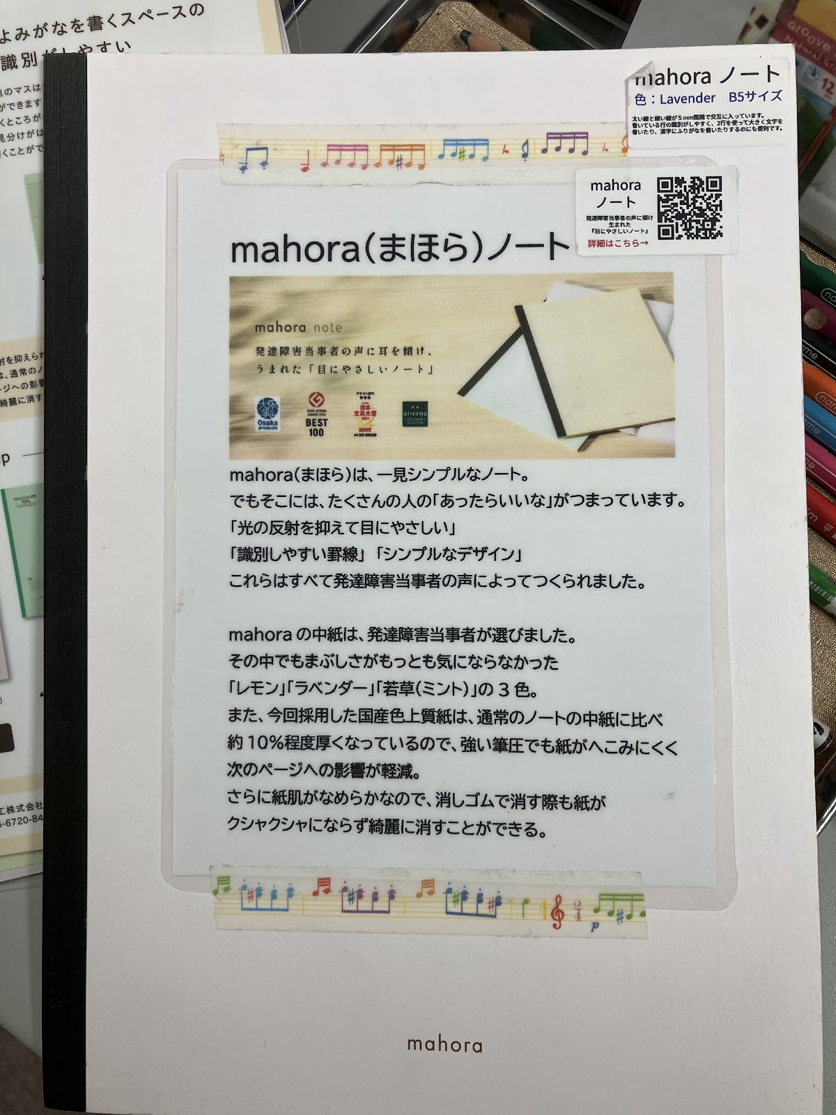 
この画像は「mahora（まほら）ノート」の商品紹介ページです。表紙には、発達障害当事者の声を元に作られた「目にやさしいノート」として、視覚的な配慮や使いやすさに関する説明があります。また、ノートの中紙は選び抜かれた国産紙を使用しており、反射を抑えて目に優しく、消しゴムで消した際にも紙がクシャクシャになりにくい点が強調されています。ノートのカラーバリエーションとして「レモン」「ラベンダー」「若草（ミント）」の3色が紹介されています。