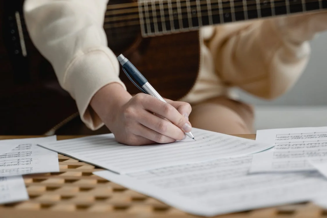 Someone holding a guitar and writing sheet music. 