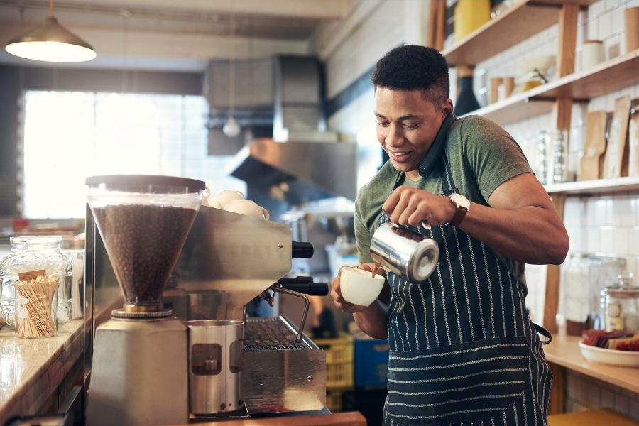 Barista pouring steamed milk into a coffee cup at a café.