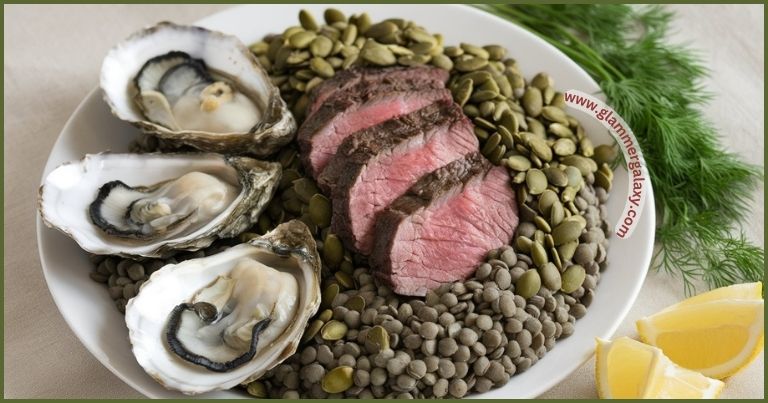 Plate of zinc-rich foods including oysters, beef, lentils, with lemon wedges