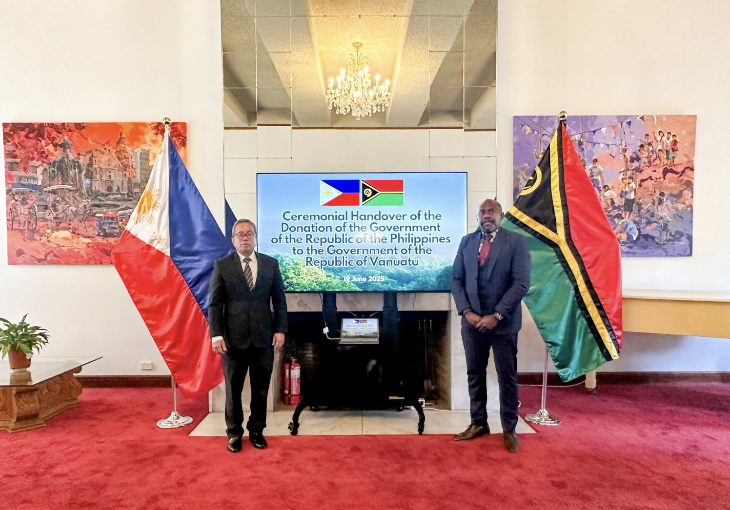 Two men standing in front of a screenDescription automatically generated