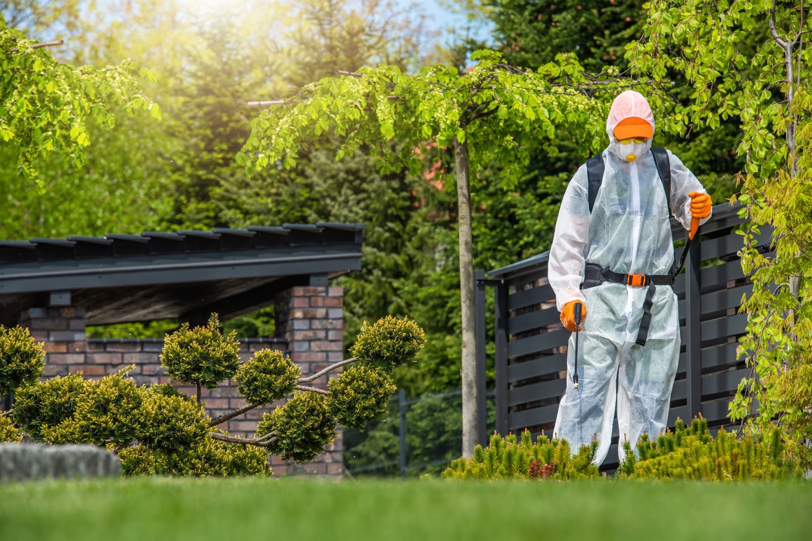 Pest control technician in protective gear applying treatment in a landscaped garden for safe pest management.