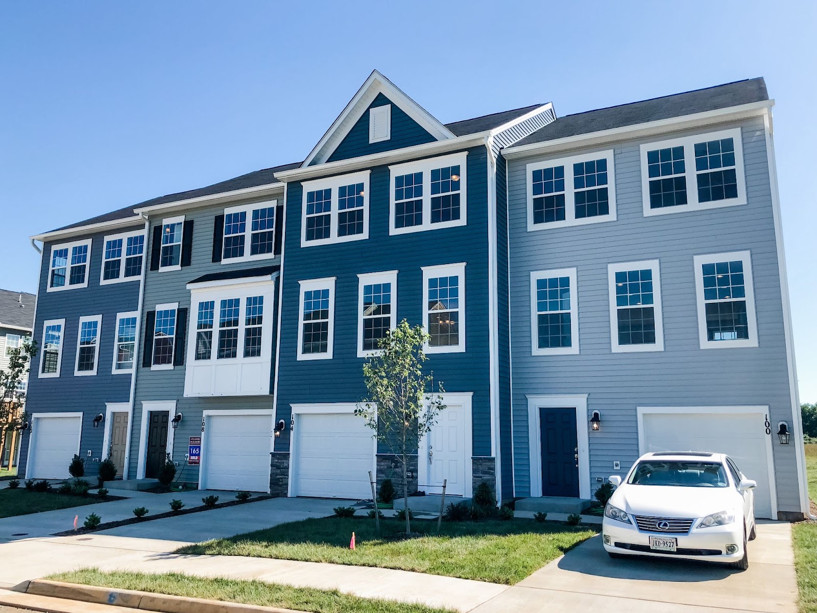 A row of newly constructed three-story townhomes with various shades of siding, windows, attached garages, and small front lawn