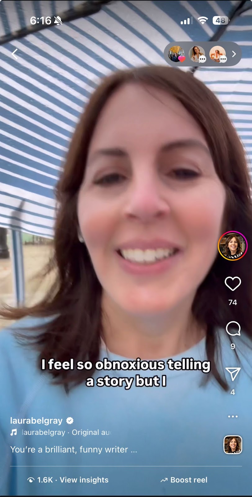 Laura Belgray with fair skin and shoulder-length brown hair is smiling slightly while recording a selfie video outdoors. She is standing under a structure with diagonal blue and white striped fabric above her, possibly a canopy or awning. On-screen captions read, “I feel so obnoxious telling a story but I.” The video appears to be a social media reel from Instagram, as indicated by the interface elements. Her username “laurabelgray” is visible at the bottom, along with the caption “You’re a brilliant, funny writer …” The post shows engagement icons including a heart with 74 likes, a comment bubble, and a paper airplane symbol. The time “6:16” and other phone status icons are visible at the top of the screen.
