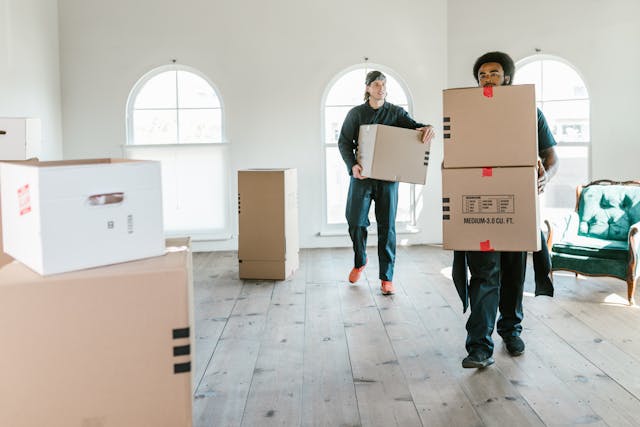 Two people moving boxes into room