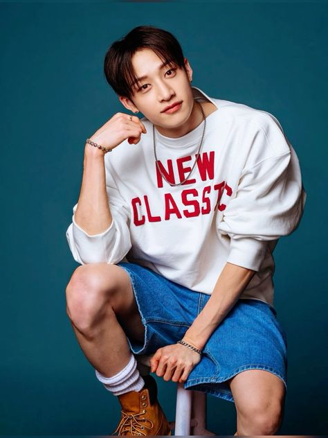 This  contain an image Bangchan  sitting on top of a chair wearing a new class shirt and shorts