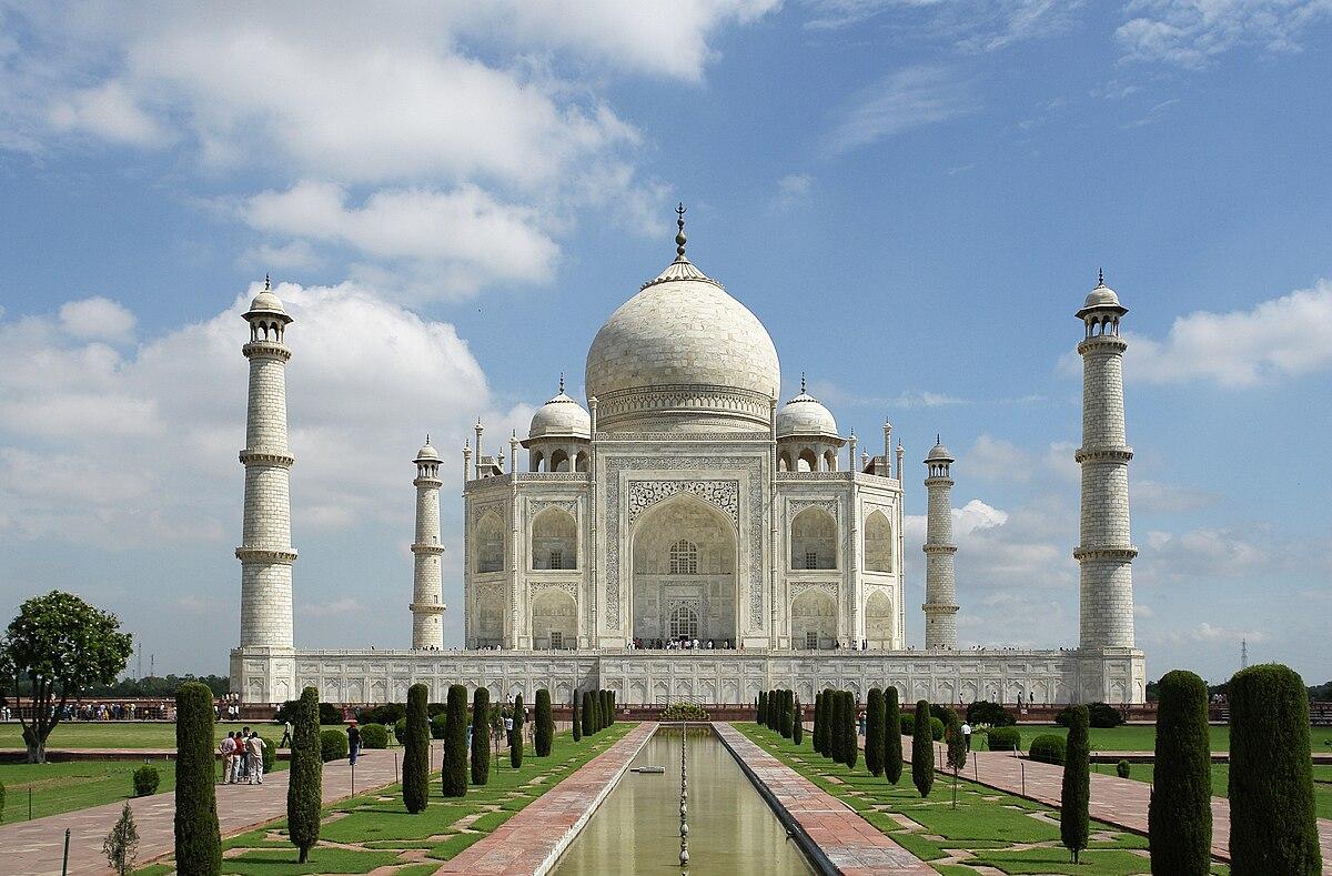 A white building with towers and a pool of water with Taj Mahal in the background

Description automatically generated