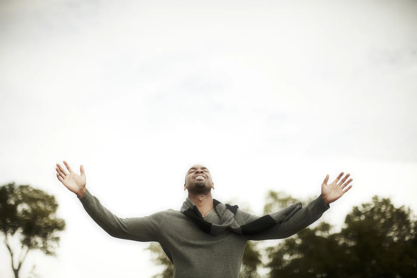 A Black man against a bright sky with his arms outstretched. He has a smile on his face and his eyes are close, face tilted up.