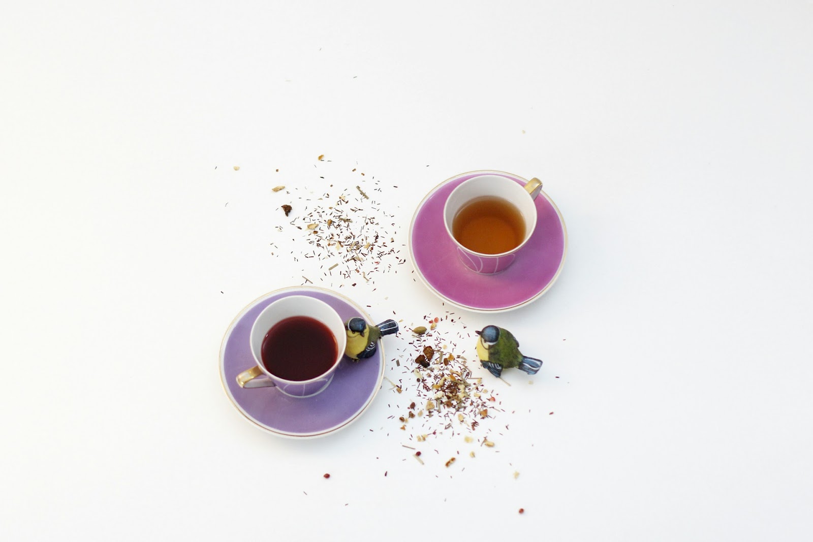 Two cups of tea with tea leaves spread around them, toy birds pretending to eat them