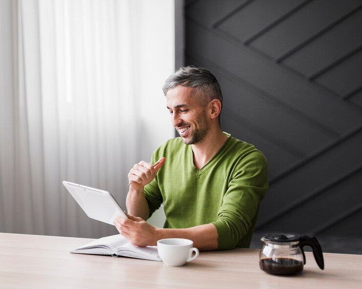 A man in a green shirt smiling while reading from a tablet.