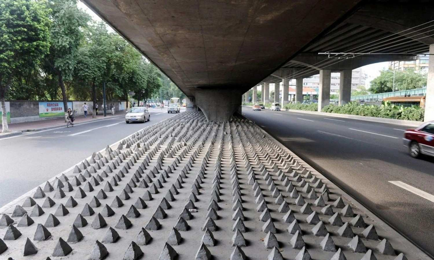 A concrete underpass, marked by hostile architecture with numerous conical spikes, covers the ground beneath.