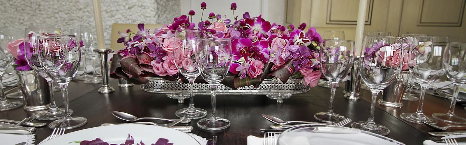 Mesa com pratos, talheres e taças com arranjo central de flores roxas