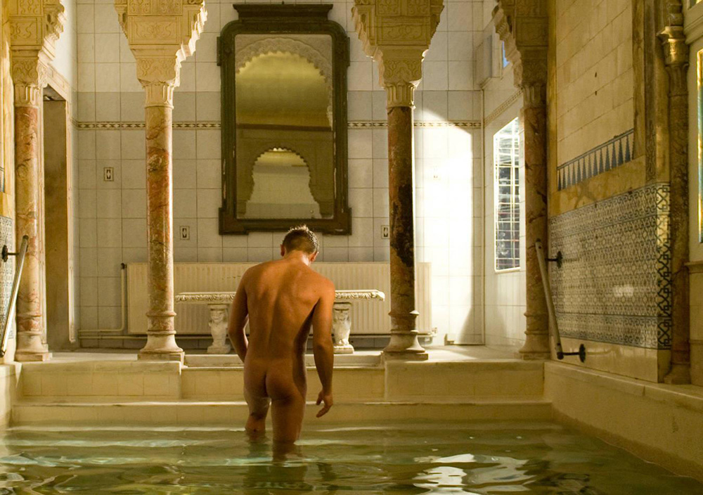 gay sauna KAISERBRÜNDL Herrensauna in Vienna, Austria with Moorish theme architecture with hot naked male stepping out of the indoor pool water surrounded by elaborate design pillars showing off gay bubble butt