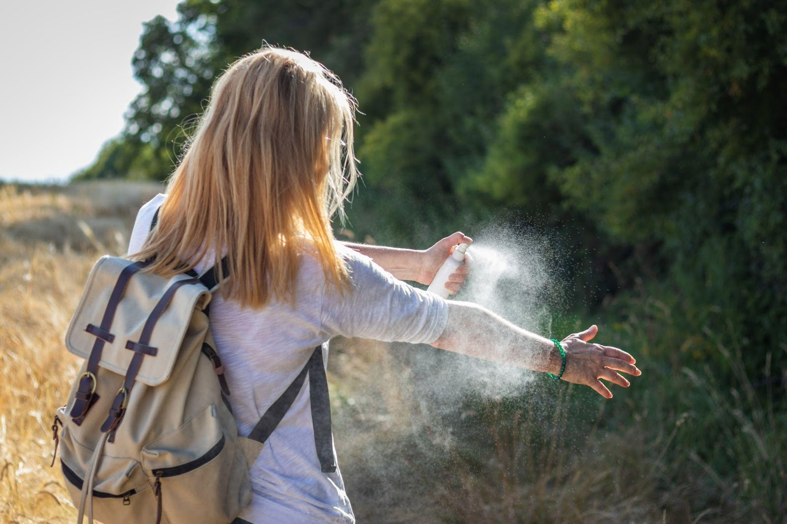 A woman applying bug spray before going on a hike.