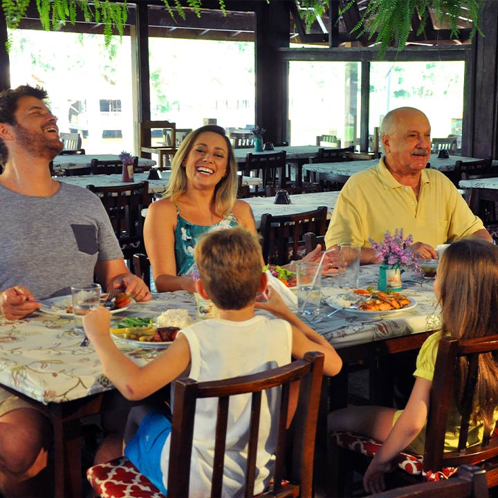 Reunião familiar alegre durante um almoço em um restaurante, com sorrisos e pratos variados sobre a mesa.