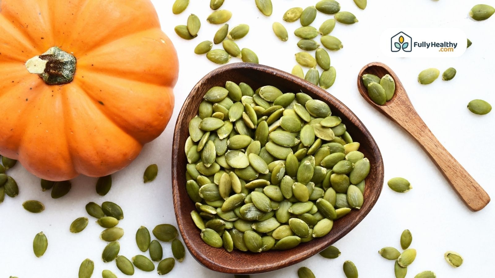 Whole pumpkin with green pumpkin seeds in bowl and wooden spoon