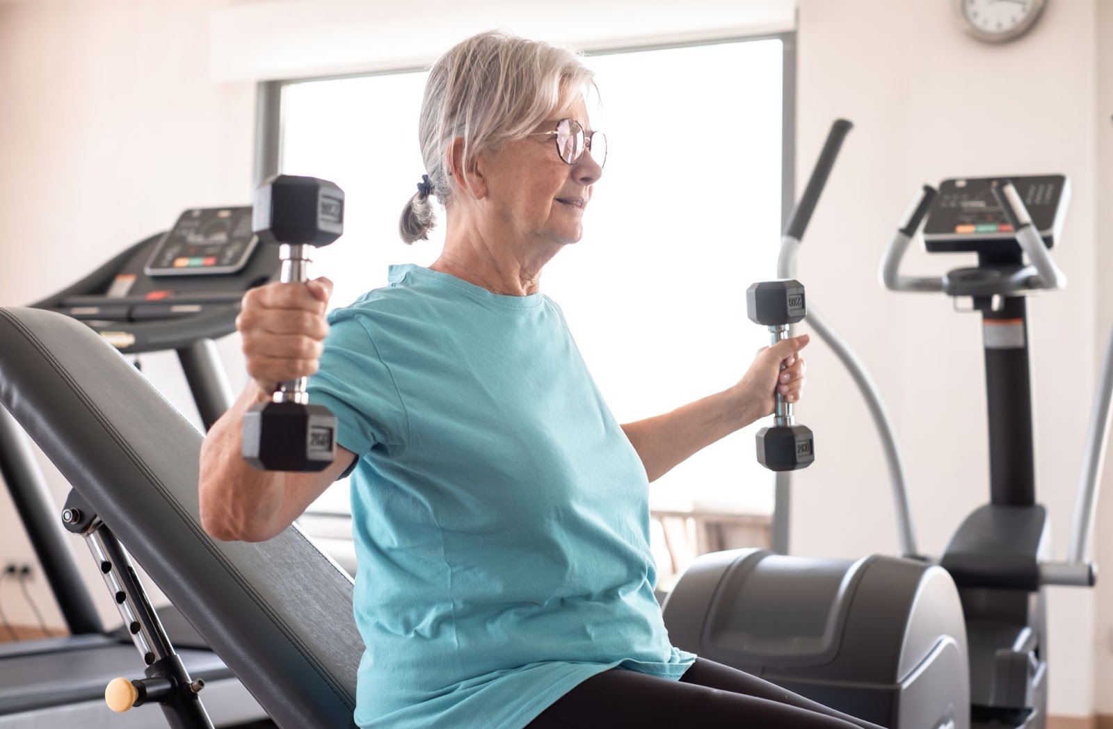 An older woman at the gym, lifting weights safely in order to avoid injury.