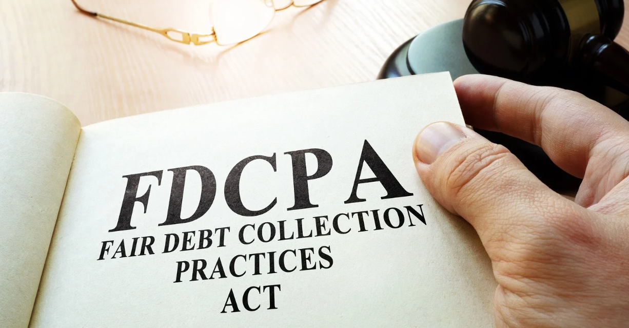 (A close-up of a person holding a booklet titled "FDCPA - Fair Debt Collection Practices Act," symbolizing consumer protection from abusive debt collection practices.)