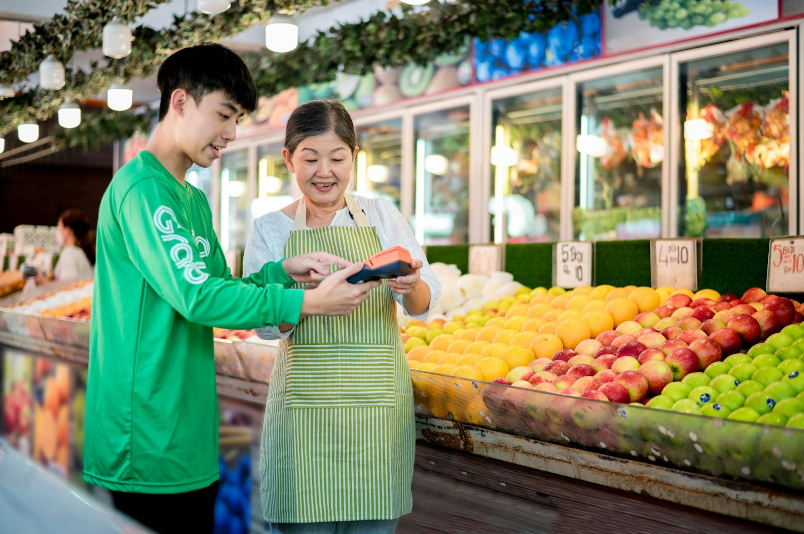 A man and woman smile as they stand together in front of a colorful fruit stand filled with fresh produce.