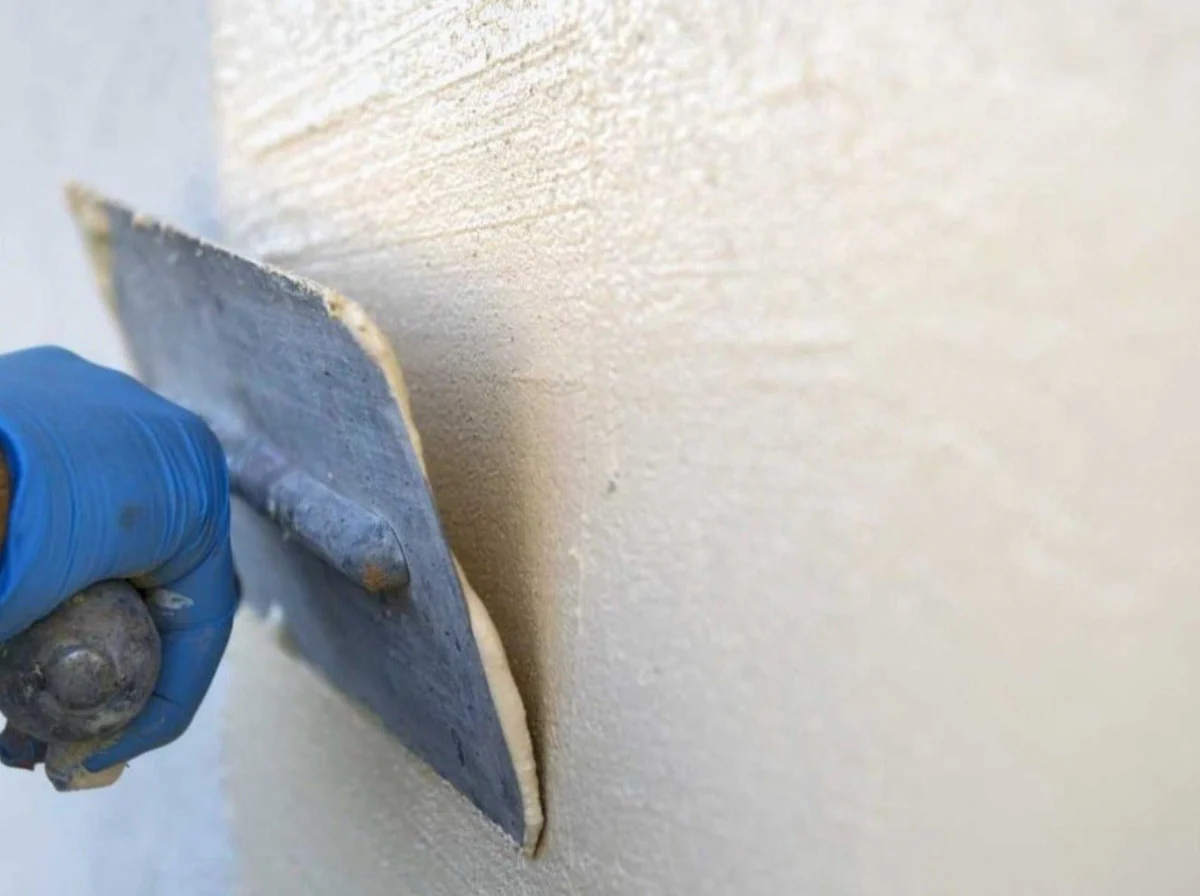 A person wearing blue gloves applies Decork Design Thermal Cork Paint to a wall.&nbsp;
