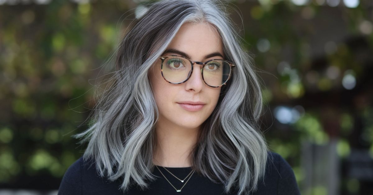 A woman with glasses and gray hair showcasing a stylish balayage for gray hair, highlighting her elegant look.