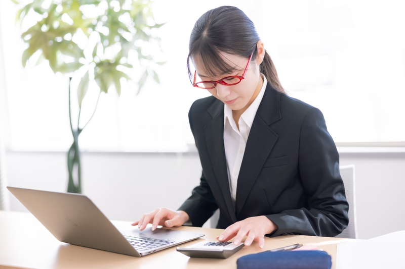 ノートPCと電卓で資料を作っているスーツ姿の女性