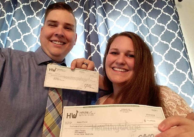 A man and a woman stand side by side as they smile and hold up checks they earned from Healthy Wage.