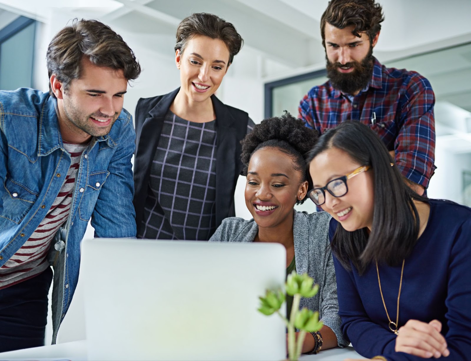 Group of professionals looking at a single laptop and smiling in an office. 