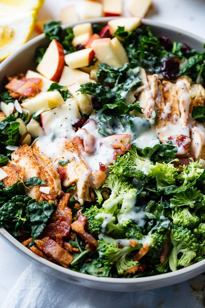 A photo of a kale salad loaded with apples, bacon, cranberries and smoked chicken topped with a poppy seed dressing.