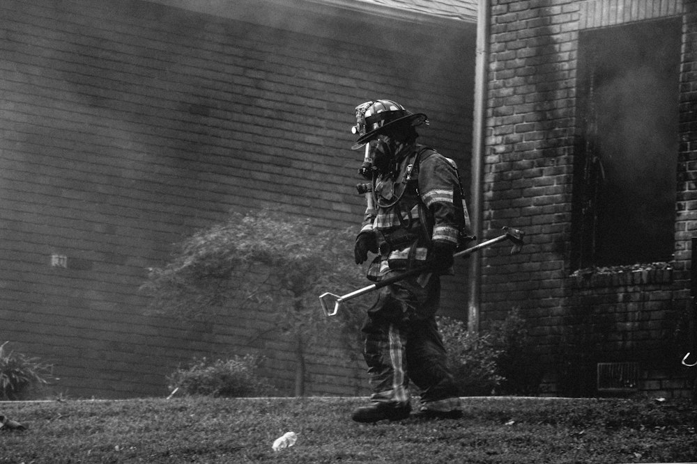 grayscale photography of firefighter holding equipment near houses