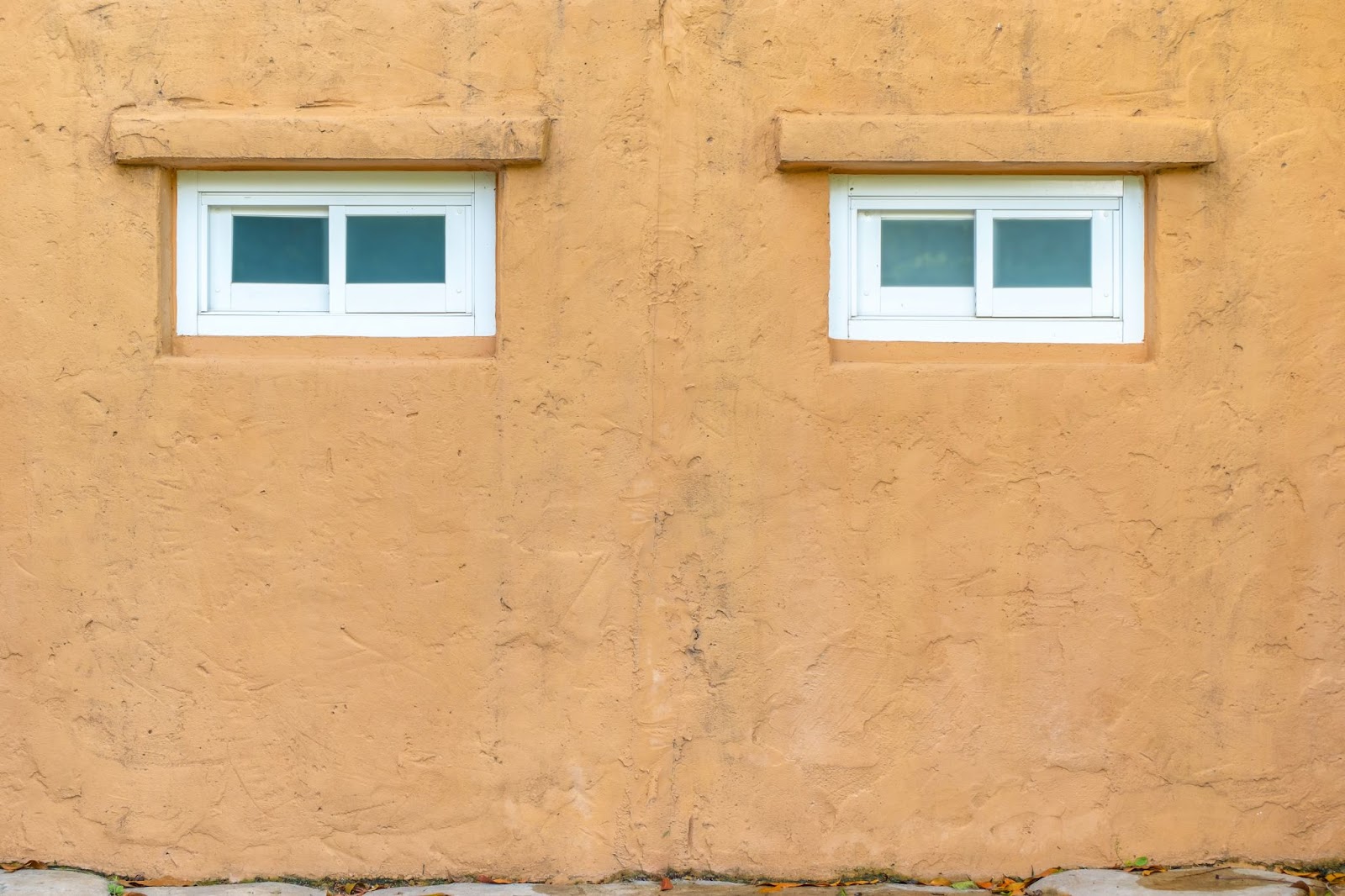 Orange stucco wall featuring two white windows.