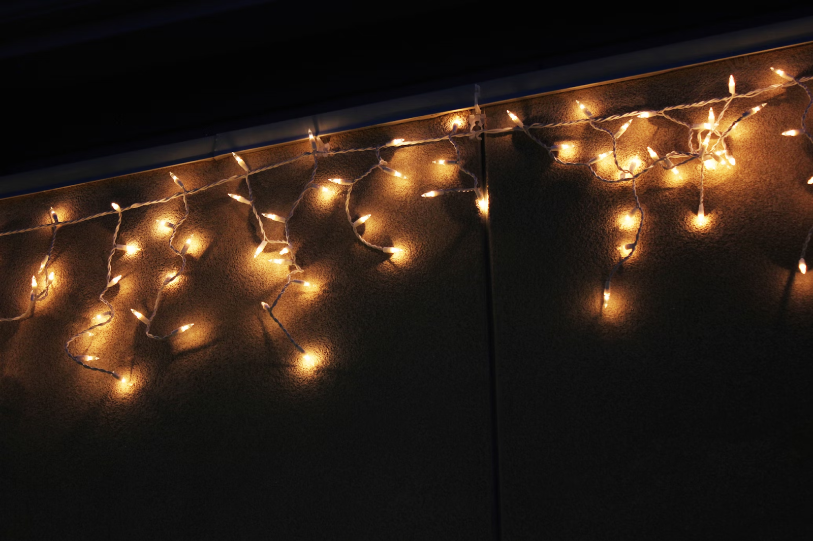 Warm white icicle Christmas lights hanging from a house during the holiday season.